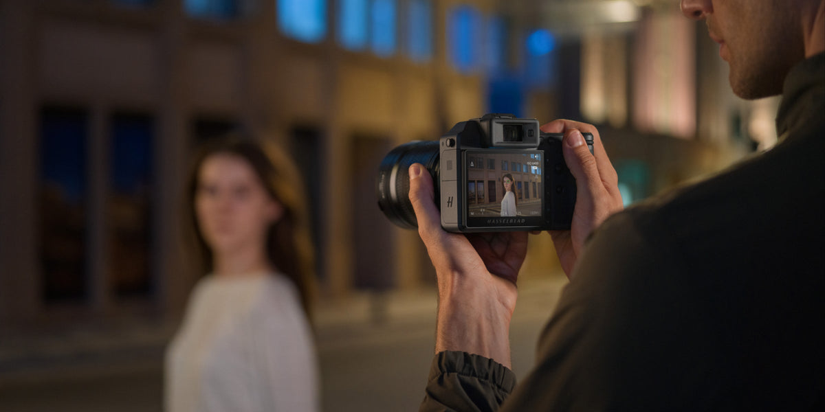 Photographer taking a portrait of a woman outdoors at night, with the camera screen in focus