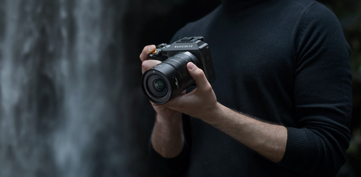 Photographer holding a Hasselblad camera with a zoom lens in front of a blurred waterfall