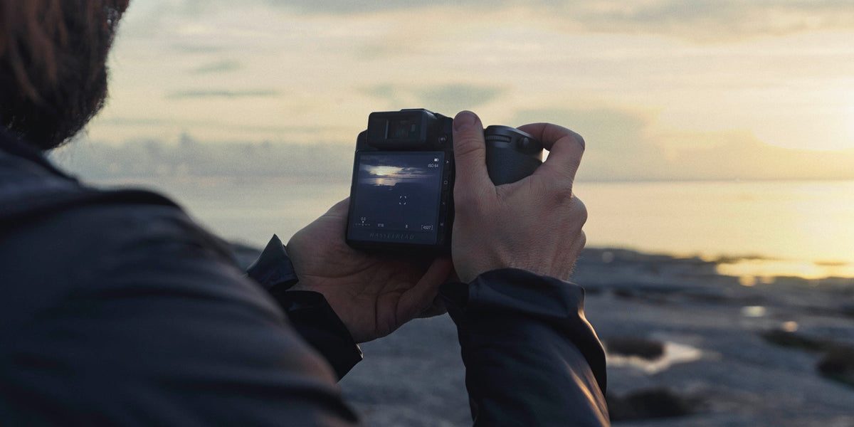 Photographer reviewing an image on a Hasselblad camera by the coast at sunset