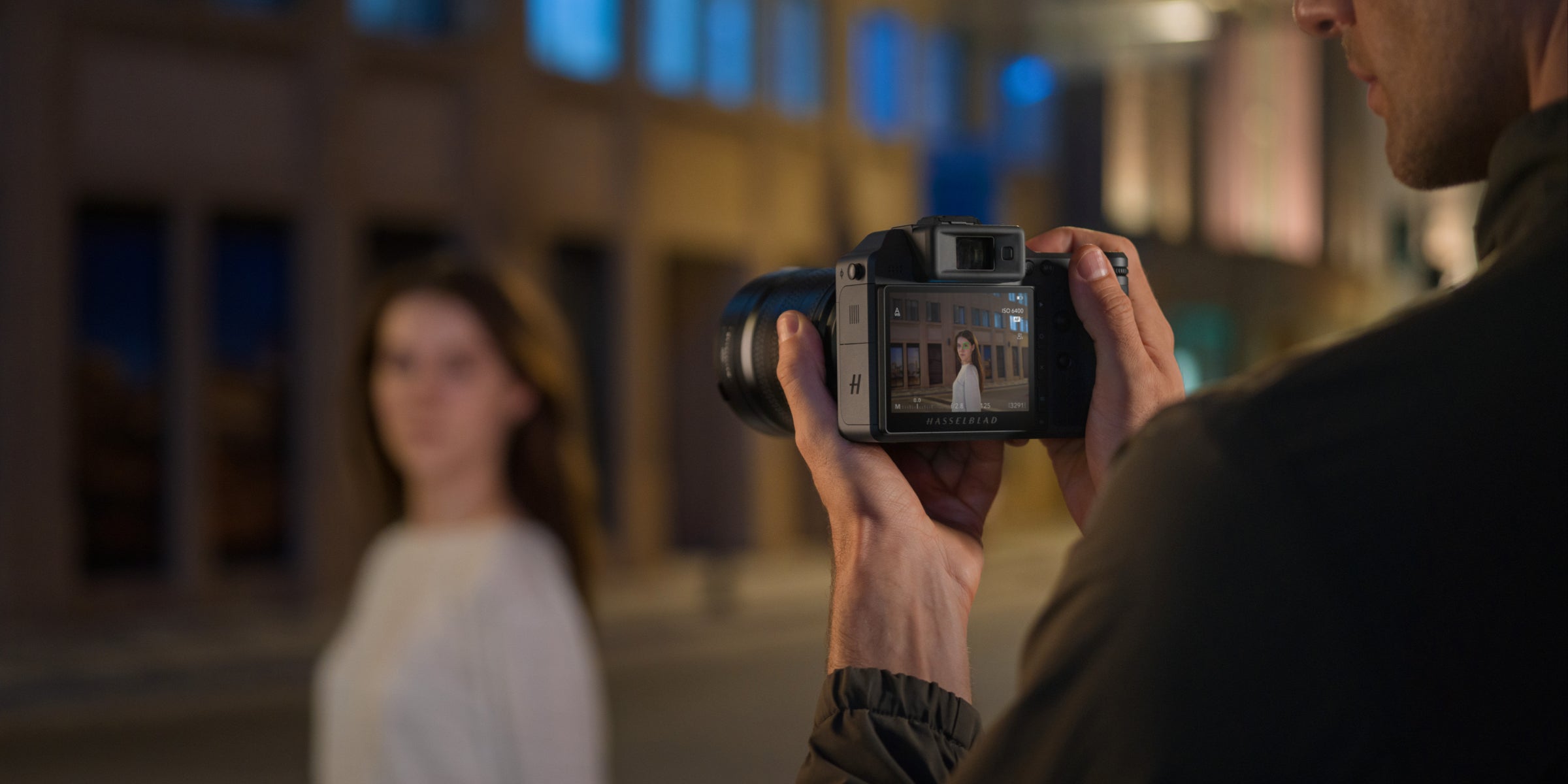Photographer taking a portrait of a woman outdoors at night, with the camera screen in focus
