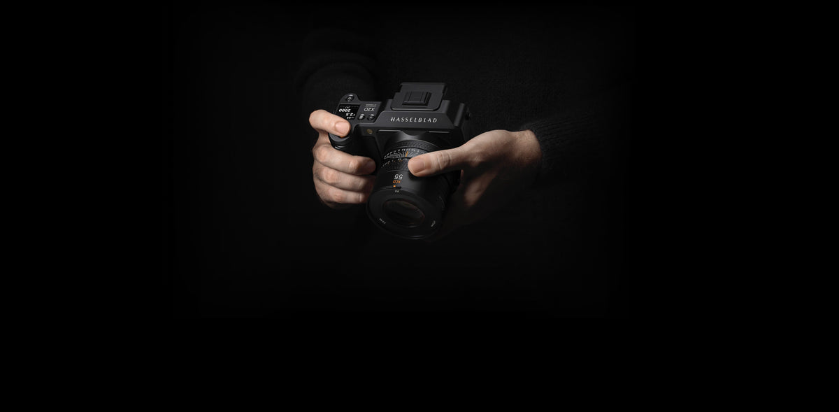 Hands holding a Hasselblad camera against a dark background 